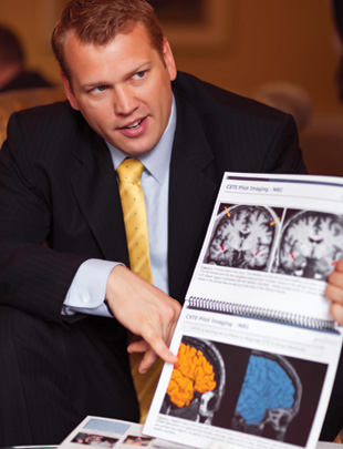 Nowinski pointing to scan of a 50-year-old former NFL player’s brain (yellow) next to a control (blue).